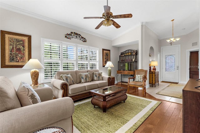 living area featuring ornamental molding, arched walkways, light wood finished floors, ceiling fan with notable chandelier, and vaulted ceiling