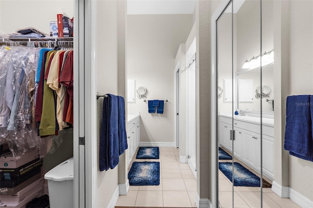 bathroom featuring vanity, baseboards, a walk in closet, tile patterned floors, and a stall shower