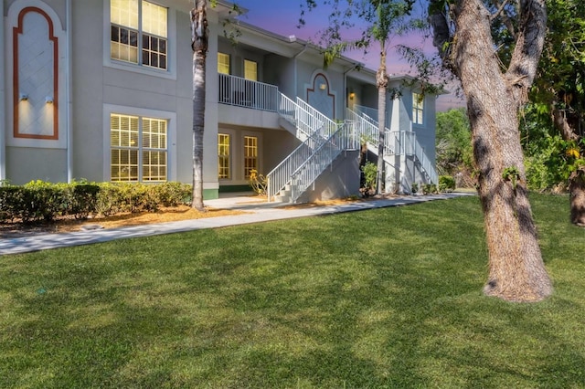 back of property with a lawn, stucco siding, and stairway