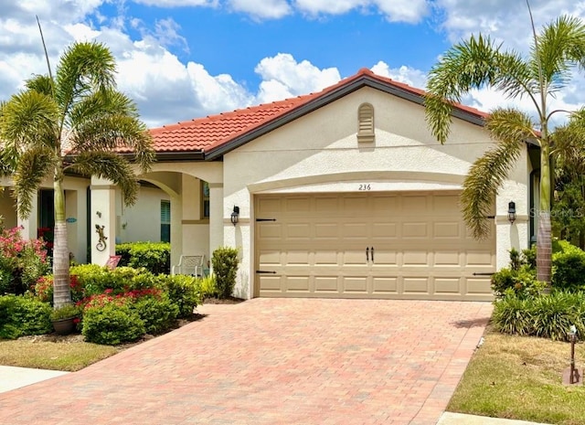 mediterranean / spanish-style home with a garage, stucco siding, a tile roof, and decorative driveway