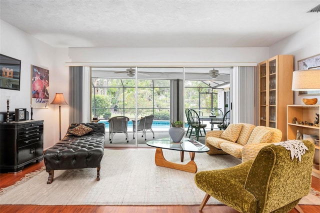 living area with a sunroom, a ceiling fan, visible vents, and wood finished floors