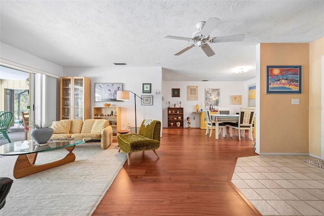 living area featuring wood finished floors, a textured ceiling, visible vents, baseboards, and ceiling fan