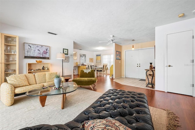 living area with ceiling fan, a textured ceiling, visible vents, and wood finished floors