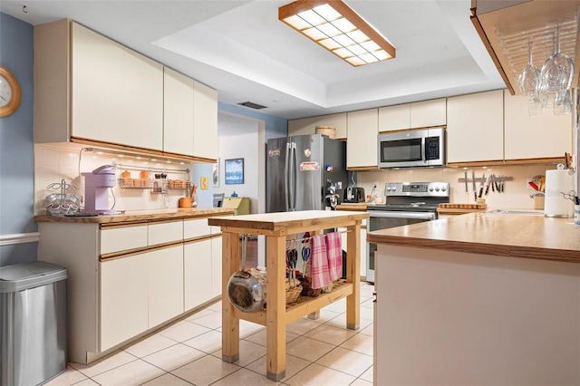 kitchen featuring stainless steel appliances, light tile patterned floors, visible vents, and a raised ceiling