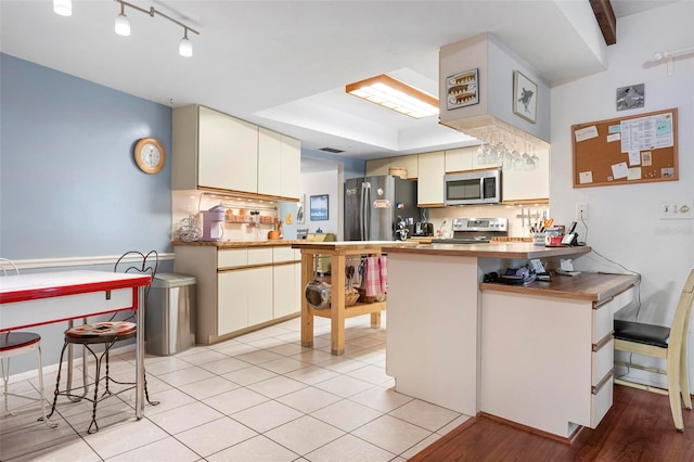 kitchen with a peninsula, stainless steel appliances, a breakfast bar, visible vents, and light wood-style flooring