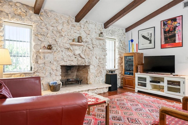 living room with visible vents, wood finished floors, lofted ceiling with beams, and a stone fireplace