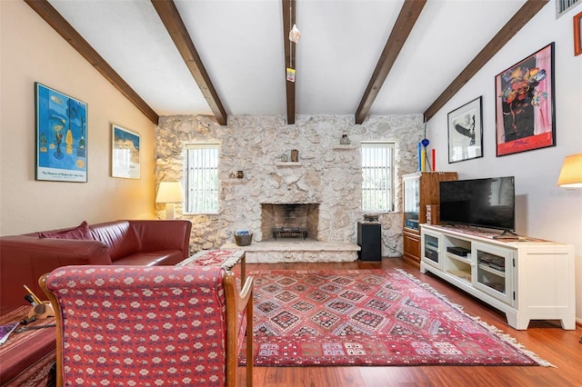 living room featuring a stone fireplace, lofted ceiling with beams, visible vents, and wood finished floors