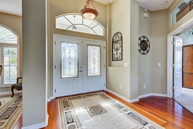 foyer entrance featuring french doors, a high ceiling, arched walkways, and wood finished floors