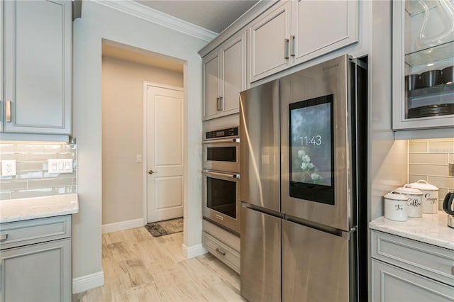 kitchen with appliances with stainless steel finishes, ornamental molding, gray cabinetry, baseboards, and tasteful backsplash