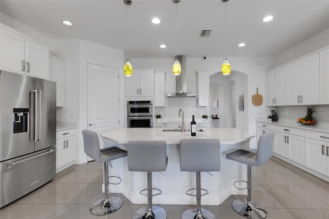 kitchen featuring visible vents, decorative backsplash, wall chimney exhaust hood, a sink, and stainless steel appliances