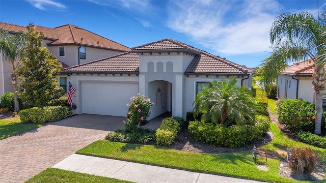 mediterranean / spanish-style house with a tiled roof, decorative driveway, an attached garage, and stucco siding