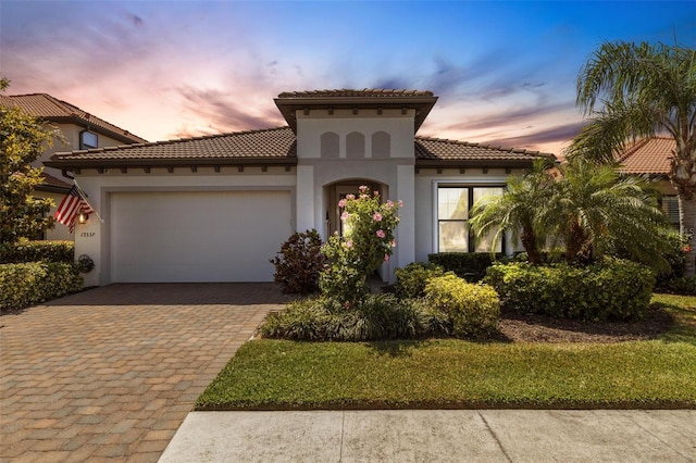 mediterranean / spanish house with decorative driveway, a garage, stucco siding, and a tile roof