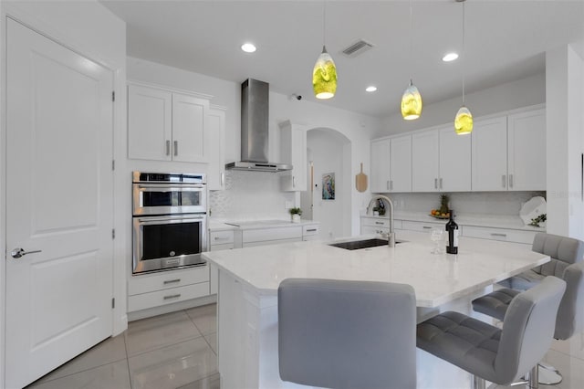 kitchen with stainless steel double oven, visible vents, arched walkways, a sink, and wall chimney exhaust hood