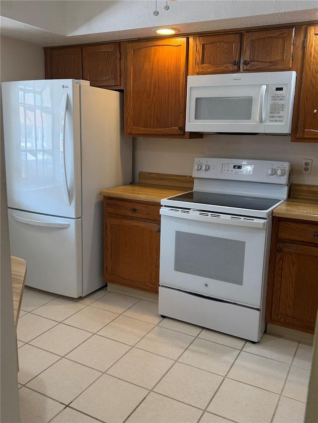 kitchen featuring light tile patterned floors, white appliances, brown cabinetry, and light countertops