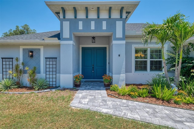view of exterior entry with stucco siding and a shingled roof