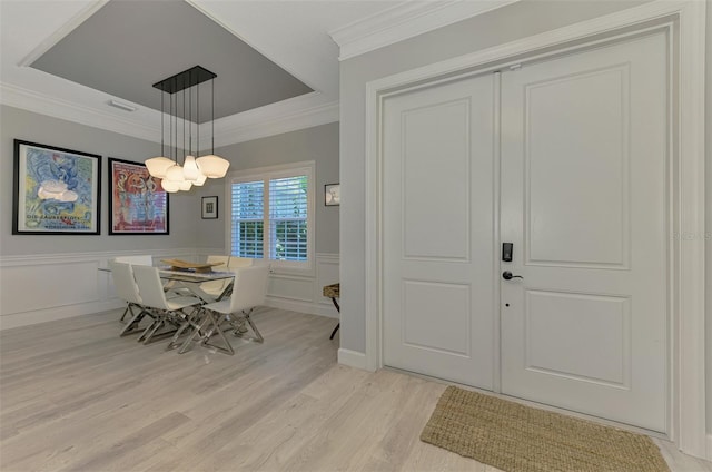 dining room featuring light wood-style floors, ornamental molding, a chandelier, a wainscoted wall, and a decorative wall