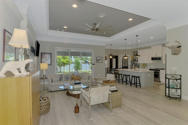 living area with ceiling fan, a tray ceiling, light wood-style floors, recessed lighting, and crown molding