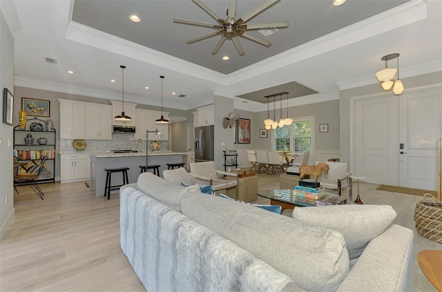 living area with a tray ceiling, ceiling fan, ornamental molding, light wood-style flooring, and recessed lighting