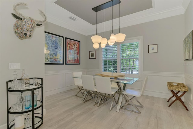 dining room featuring light wood-style floors, wainscoting, a decorative wall, ornamental molding, and a raised ceiling