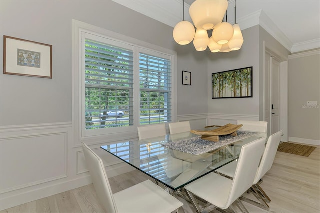 dining space featuring ornamental molding, a chandelier, light wood-style flooring, a wainscoted wall, and a decorative wall