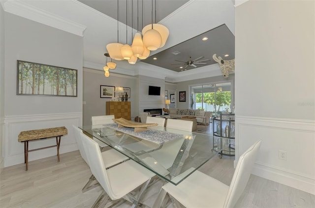 dining room featuring a tray ceiling, a ceiling fan, crown molding, wood finished floors, and a wainscoted wall