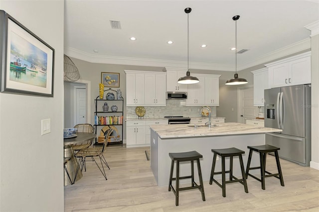 kitchen featuring appliances with stainless steel finishes, a sink, white cabinetry, a kitchen bar, and crown molding