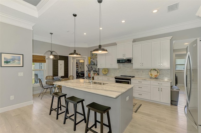 kitchen with appliances with stainless steel finishes, a sink, light wood-style flooring, decorative backsplash, and a breakfast bar area