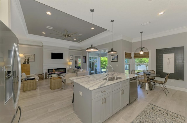 kitchen with a sink, appliances with stainless steel finishes, a ceiling fan, a glass covered fireplace, and light stone countertops