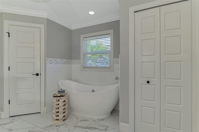 bathroom with a closet, marble look tile flooring, a freestanding tub, wainscoting, and ornamental molding
