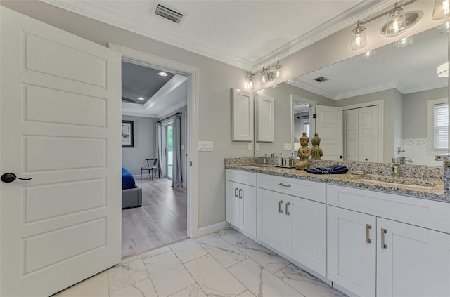 bathroom with healthy amount of natural light, double vanity, ornamental molding, baseboards, and marble look tiles