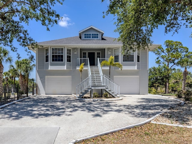 coastal home featuring covered porch, stairs, a garage, and driveway