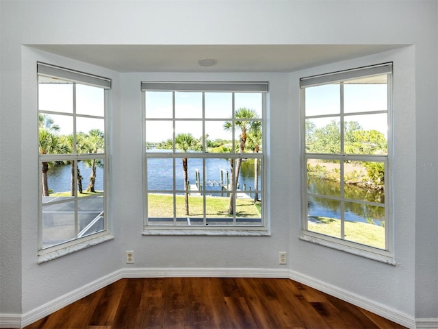 interior space featuring plenty of natural light, a water view, baseboards, and dark wood-style floors