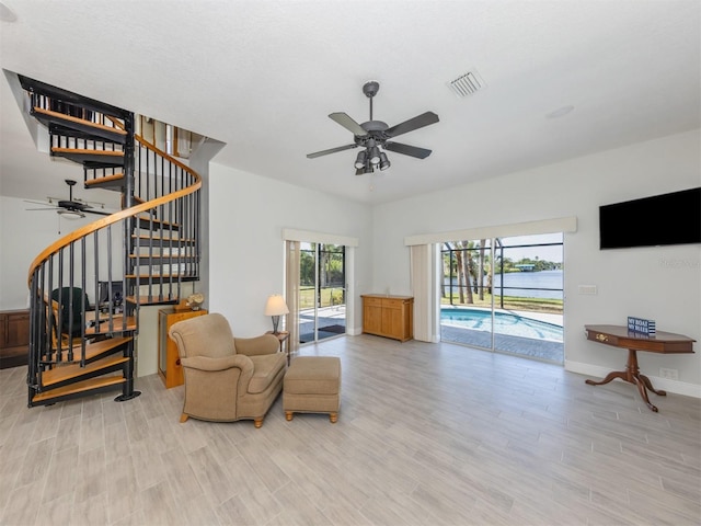 living area featuring wood finished floors, a ceiling fan, visible vents, baseboards, and stairs