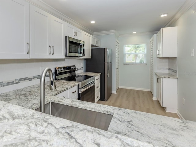 kitchen with appliances with stainless steel finishes, crown molding, a sink, decorative backsplash, and white cabinets