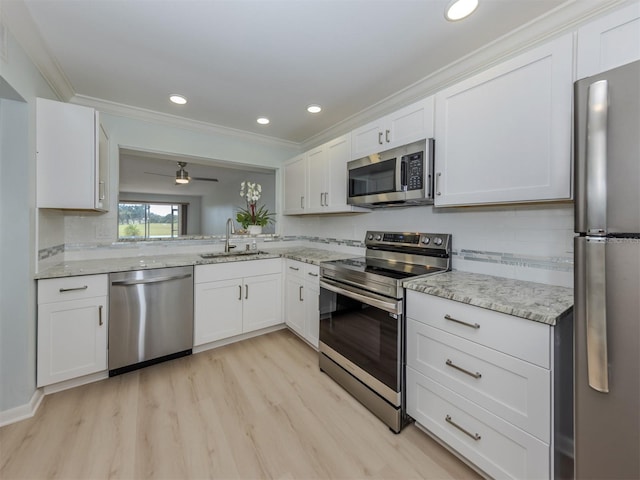 kitchen with appliances with stainless steel finishes, a sink, light wood-type flooring, crown molding, and white cabinets