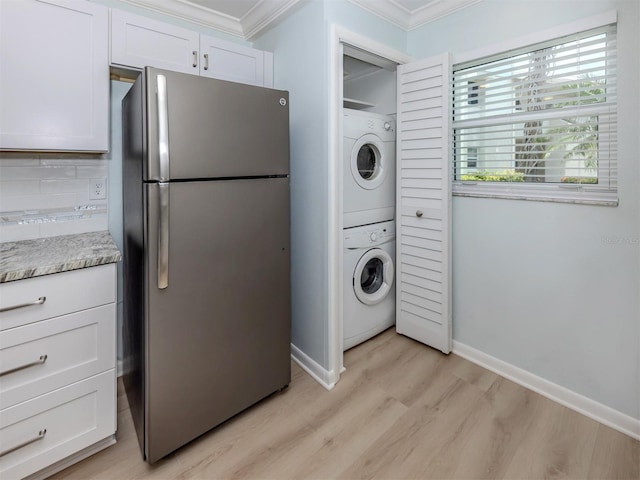 clothes washing area featuring stacked washer / dryer, ornamental molding, light wood-type flooring, and baseboards