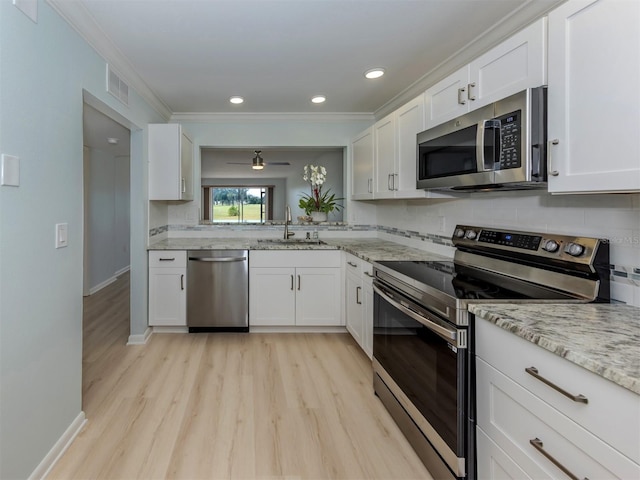 kitchen with appliances with stainless steel finishes, a sink, light wood finished floors, white cabinets, and crown molding
