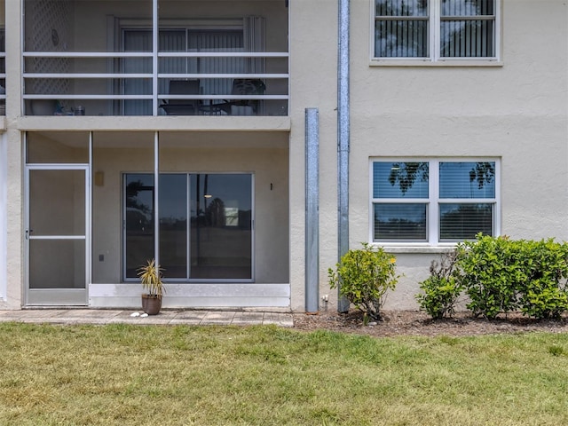 back of house with stucco siding, a lawn, and a balcony