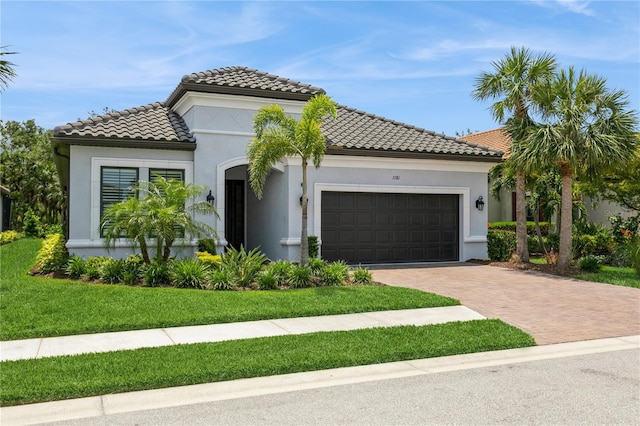 mediterranean / spanish home featuring a garage, decorative driveway, a tile roof, stucco siding, and a front lawn