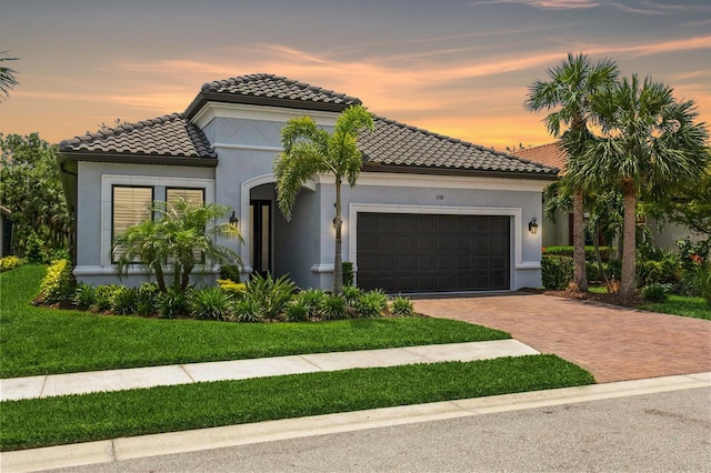 mediterranean / spanish-style house featuring decorative driveway, an attached garage, a tile roof, stucco siding, and a lawn
