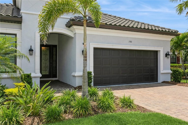 property entrance with a tiled roof, stucco siding, driveway, and a garage