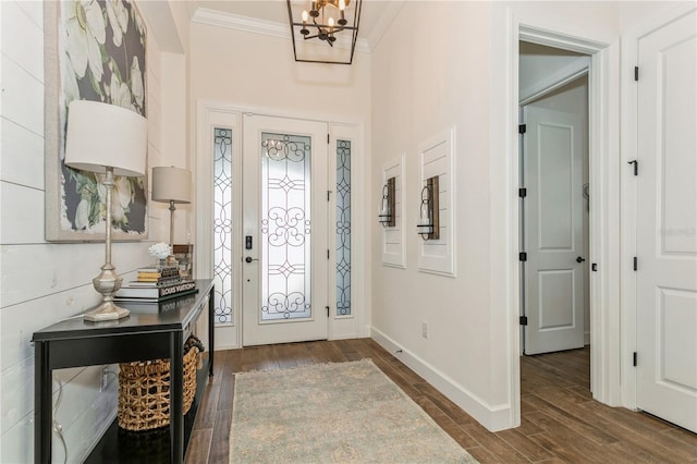 entrance foyer with dark wood-style flooring, ornamental molding, a chandelier, and baseboards