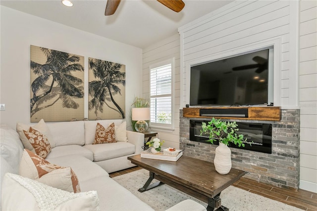 living area with a glass covered fireplace, a ceiling fan, and wood finished floors