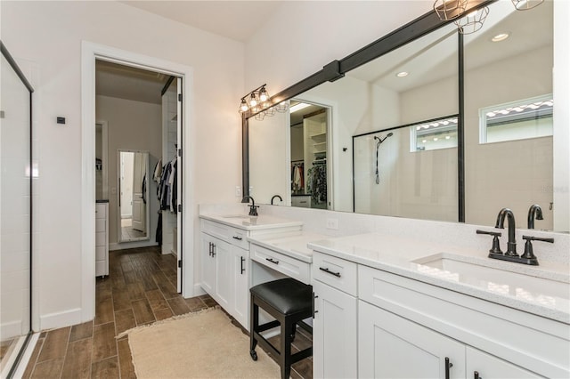 bathroom with a stall shower, a spacious closet, double vanity, wood finish floors, and baseboards