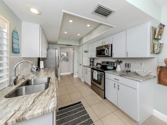 kitchen with stainless steel appliances, a sink, tasteful backsplash, a raised ceiling, and recessed lighting
