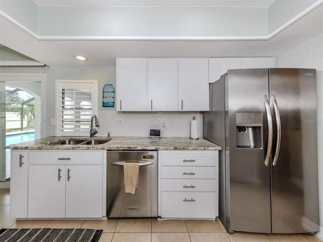 kitchen with appliances with stainless steel finishes, a sink, light tile patterned flooring, white cabinetry, and light stone countertops
