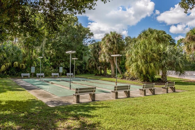 view of community featuring a lawn, shuffleboard, and view of wooded area