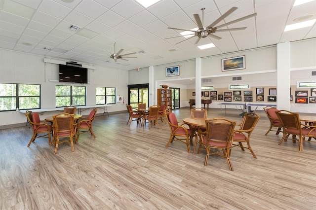 dining area with a ceiling fan, light wood-style floors, a towering ceiling, a drop ceiling, and baseboards