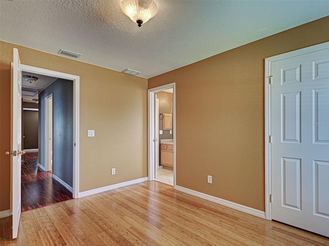 4103 Kinlock St, North Port, FL 34286 - unfurnished bedroom featuring light wood-style floors, a textured ceiling, a textured wall, and ensuite bath