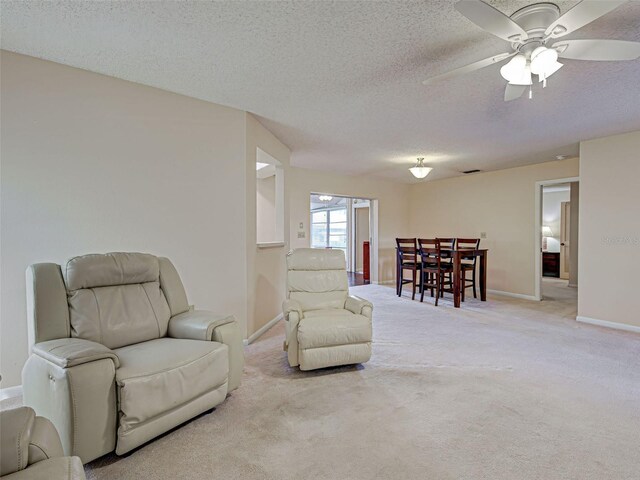 sitting room featuring a textured ceiling, baseboards, light colored carpet, and ceiling fan